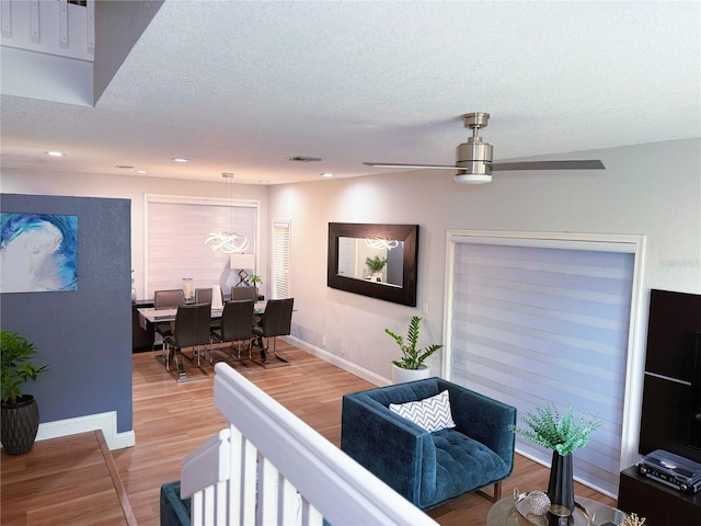 living room featuring a textured ceiling, ceiling fan, visible vents, baseboards, and light wood finished floors