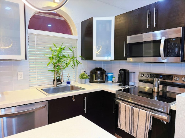 kitchen with stainless steel appliances, light countertops, backsplash, a sink, and dark cabinets