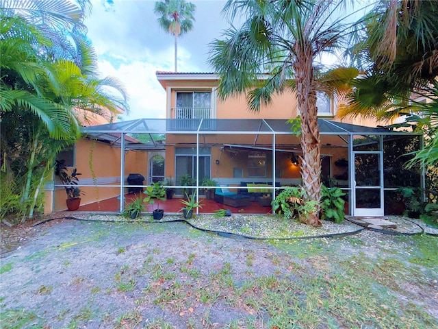 rear view of property featuring glass enclosure, a patio, and stucco siding