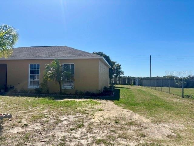 view of side of property with a yard, roof with shingles, fence, and stucco siding