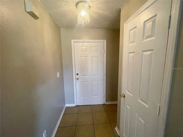 hallway with dark tile patterned floors, baseboards, and a textured ceiling