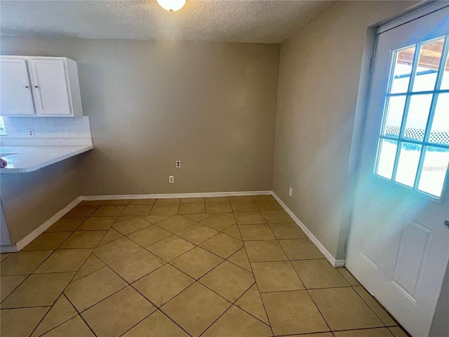 unfurnished dining area with light tile patterned floors, a textured ceiling, and baseboards