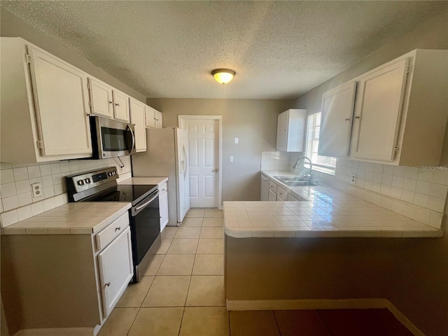 kitchen with appliances with stainless steel finishes, tile counters, a sink, and a peninsula