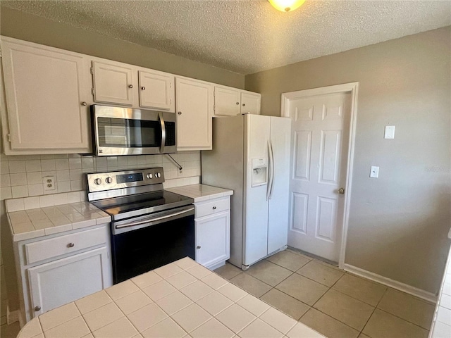 kitchen with tile countertops, light tile patterned floors, stainless steel appliances, white cabinetry, and backsplash