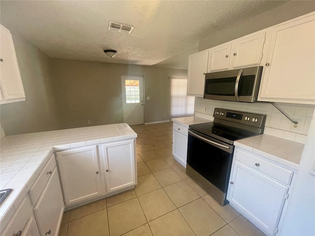 kitchen featuring stainless steel appliances, tile counters, visible vents, white cabinets, and a peninsula