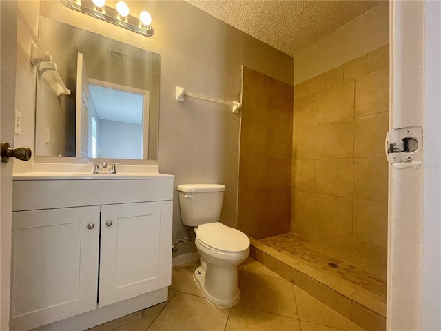 bathroom with toilet, a tile shower, vanity, a textured ceiling, and tile patterned floors