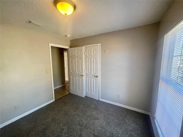 unfurnished bedroom featuring a textured ceiling, dark colored carpet, visible vents, and baseboards