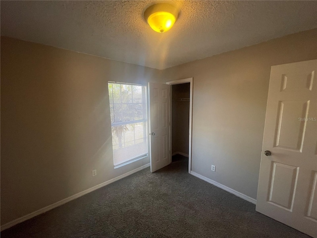 unfurnished bedroom featuring dark colored carpet, a closet, a textured ceiling, and baseboards