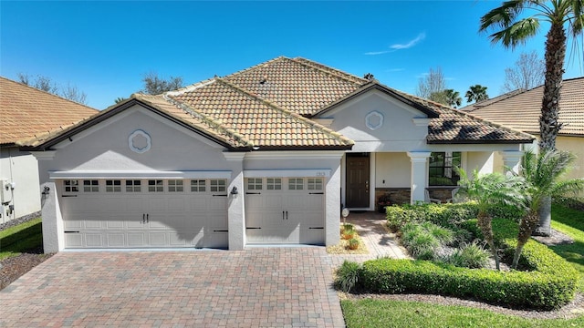 mediterranean / spanish-style home with a garage, a tile roof, stone siding, decorative driveway, and stucco siding