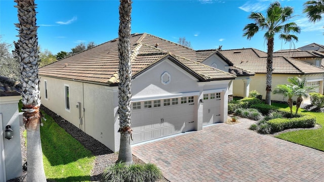 view of front facade with a garage, decorative driveway, a tile roof, and stucco siding