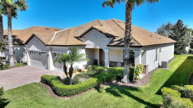 mediterranean / spanish home with a garage, central AC unit, a tiled roof, decorative driveway, and a front yard