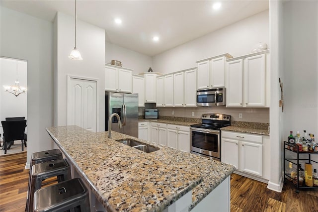 kitchen with a breakfast bar area, stainless steel appliances, a sink, white cabinets, and dark wood-style floors