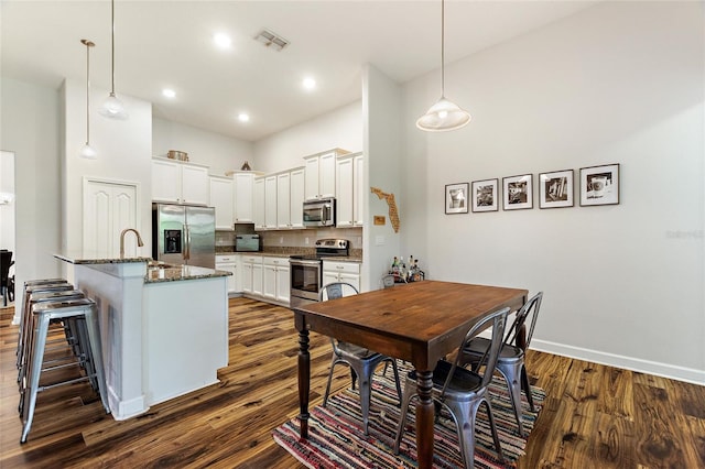 dining room with dark wood-type flooring, a high ceiling, visible vents, and baseboards