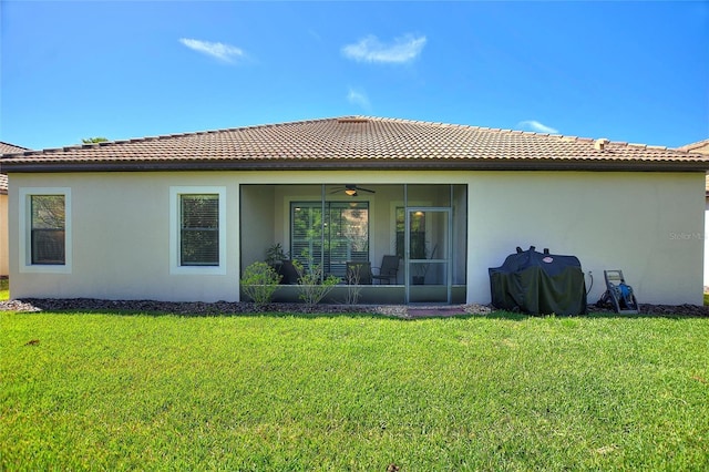 back of house with stucco siding, a lawn, a sunroom, ceiling fan, and a tiled roof