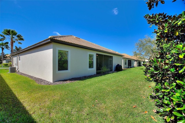 rear view of house with central AC unit, a lawn, a tile roof, and stucco siding