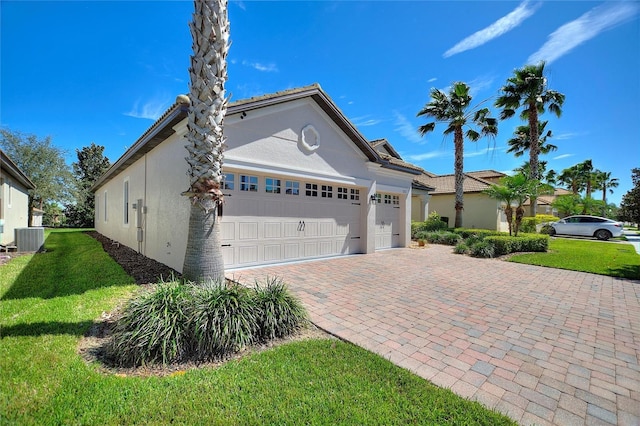 view of front of house featuring decorative driveway, stucco siding, a garage, cooling unit, and a front lawn