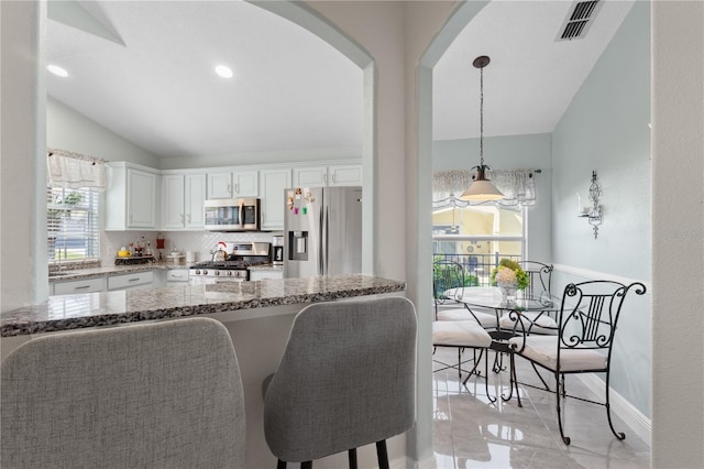 kitchen with visible vents, lofted ceiling, stainless steel appliances, stone counters, and white cabinetry