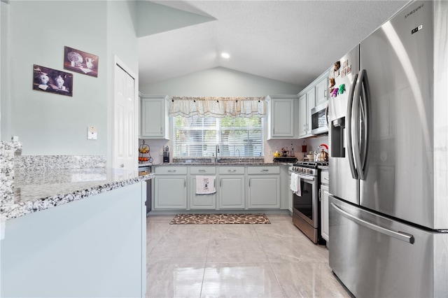 kitchen featuring light stone counters, light tile patterned floors, stainless steel appliances, a sink, and vaulted ceiling