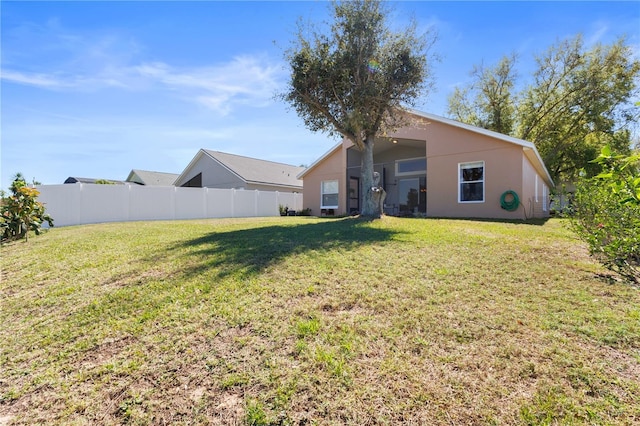 rear view of property with a yard, fence, and stucco siding