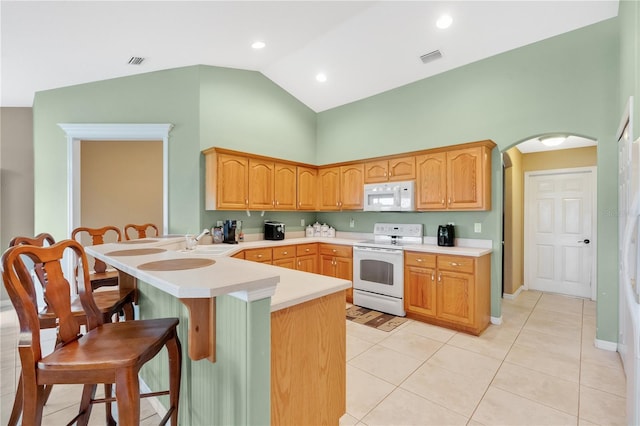 kitchen with white appliances, a peninsula, light countertops, a kitchen bar, and a sink