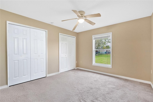 unfurnished bedroom with carpet floors, a ceiling fan, baseboards, and multiple closets