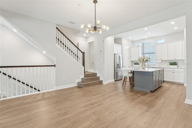 kitchen with light countertops, white cabinets, light wood-style floors, stainless steel refrigerator with ice dispenser, and a center island