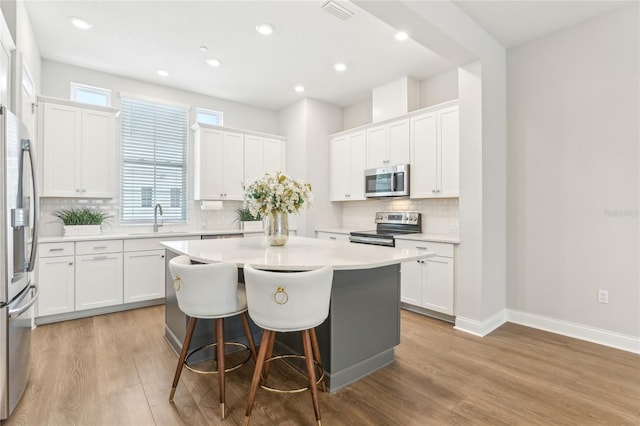 kitchen featuring a kitchen island, a sink, white cabinets, appliances with stainless steel finishes, and light wood-type flooring