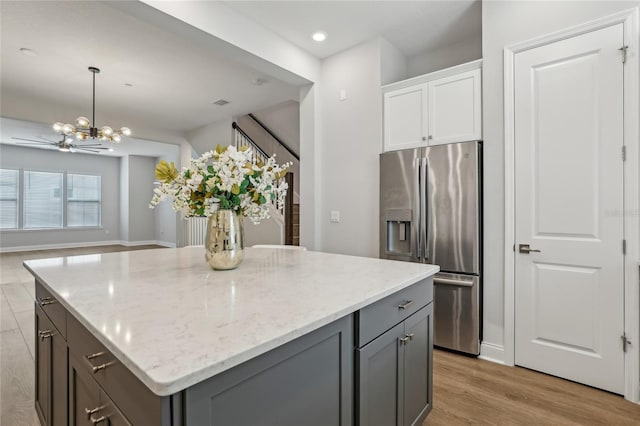 kitchen with light wood finished floors, gray cabinetry, light stone counters, an inviting chandelier, and stainless steel fridge