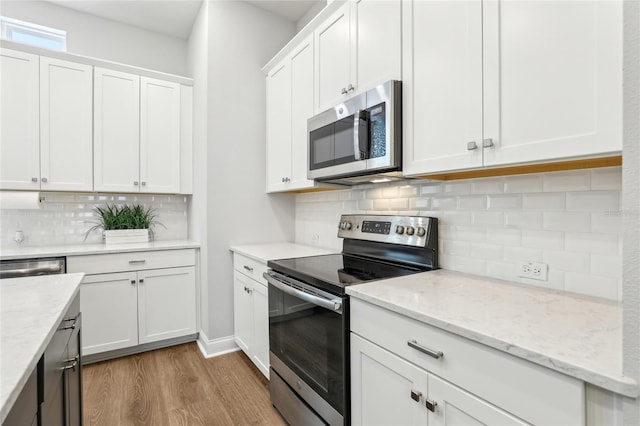 kitchen with light stone counters, appliances with stainless steel finishes, white cabinetry, light wood-type flooring, and backsplash