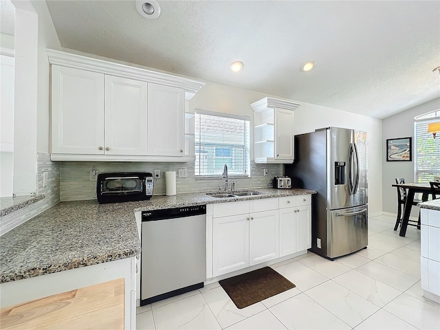 kitchen with white cabinets, a sink, a healthy amount of sunlight, stainless steel fridge, and dishwasher