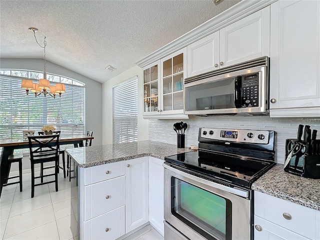 kitchen featuring lofted ceiling, a peninsula, visible vents, appliances with stainless steel finishes, and glass insert cabinets