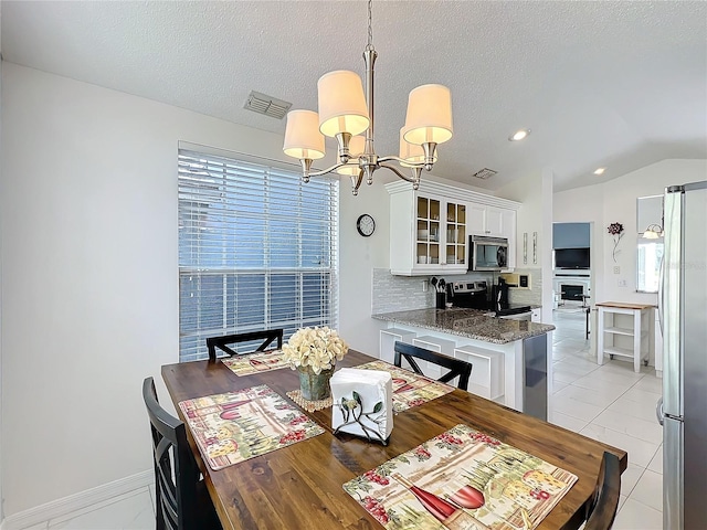 dining space with light tile patterned floors, visible vents, vaulted ceiling, a wealth of natural light, and an inviting chandelier