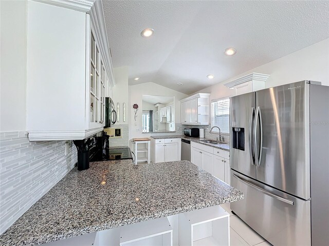 kitchen with a peninsula, light stone countertops, stainless steel appliances, open shelves, and a sink