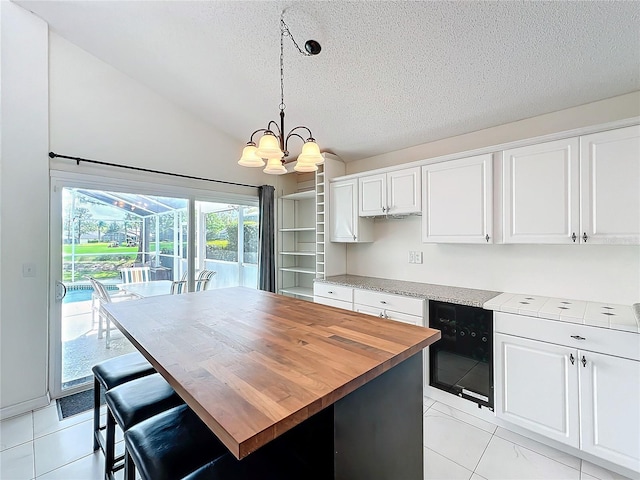 kitchen with a textured ceiling, a chandelier, white cabinets, vaulted ceiling, and wooden counters