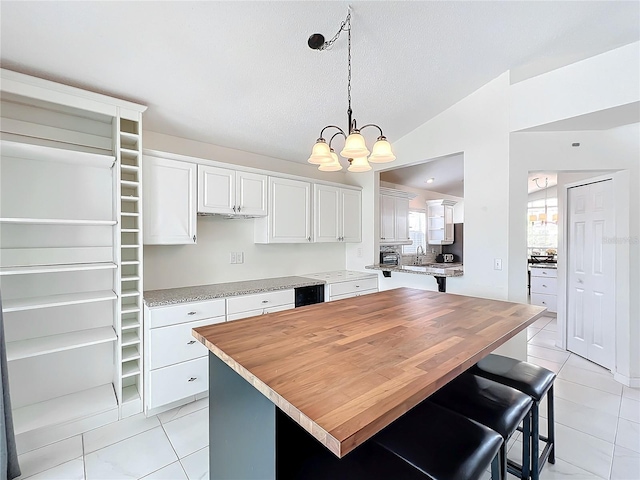 kitchen featuring decorative light fixtures, a notable chandelier, light tile patterned floors, lofted ceiling, and white cabinets