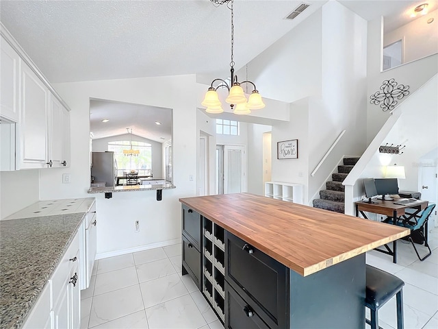 kitchen featuring butcher block countertops, visible vents, a kitchen breakfast bar, freestanding refrigerator, and an inviting chandelier