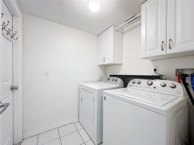 laundry area featuring washer and clothes dryer, light tile patterned floors, cabinet space, a textured ceiling, and baseboards