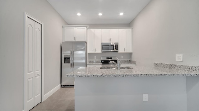 kitchen featuring light tile patterned flooring, a peninsula, white cabinetry, appliances with stainless steel finishes, and light stone countertops