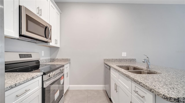 kitchen with light tile patterned flooring, stainless steel appliances, a sink, baseboards, and light stone countertops