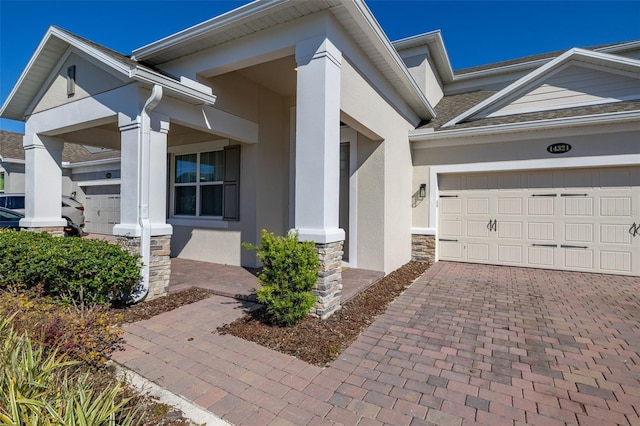 entrance to property with stone siding, stucco siding, decorative driveway, and covered porch