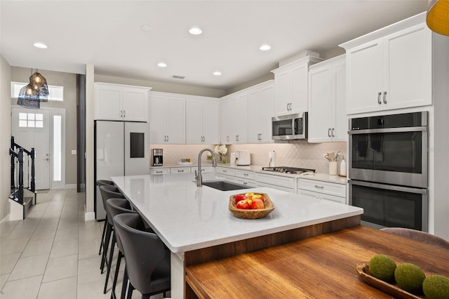 kitchen with a sink, white cabinetry, stainless steel appliances, a breakfast bar area, and decorative backsplash