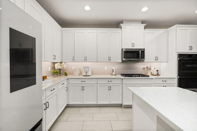 kitchen with gas stovetop, dobule oven black, white cabinetry, stainless steel microwave, and backsplash