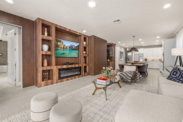 living area featuring visible vents, wooden walls, built in features, light tile patterned floors, and a glass covered fireplace