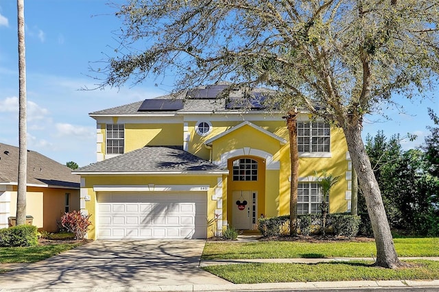 traditional-style home featuring roof with shingles, solar panels, stucco siding, an attached garage, and driveway