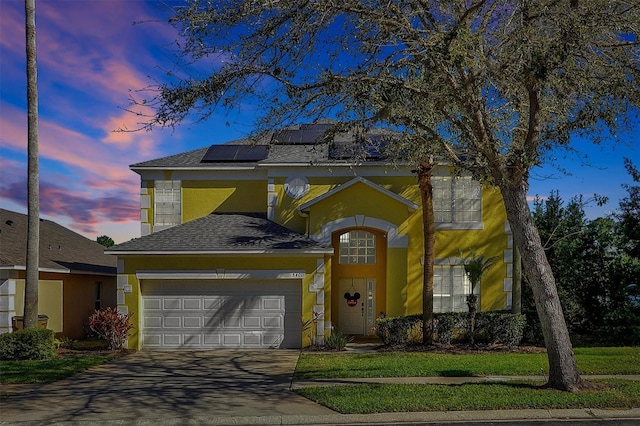 traditional-style home featuring a garage, solar panels, driveway, and stucco siding