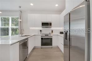 kitchen with light wood-style flooring, white cabinets, light countertops, appliances with stainless steel finishes, and modern cabinets