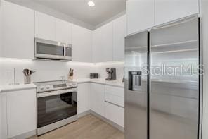 kitchen with appliances with stainless steel finishes, light countertops, light wood-type flooring, and white cabinets