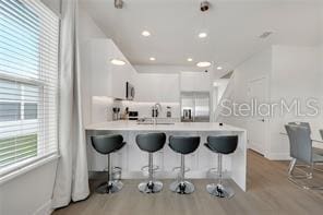 kitchen featuring stainless steel fridge, a kitchen breakfast bar, a peninsula, light countertops, and light wood-style floors