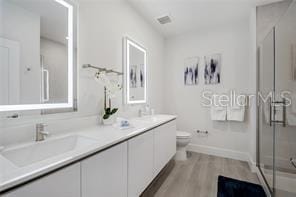 full bathroom featuring toilet, wood finished floors, a sink, double vanity, and a stall shower