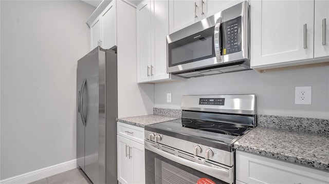 kitchen with light tile patterned floors, appliances with stainless steel finishes, white cabinetry, and light stone countertops